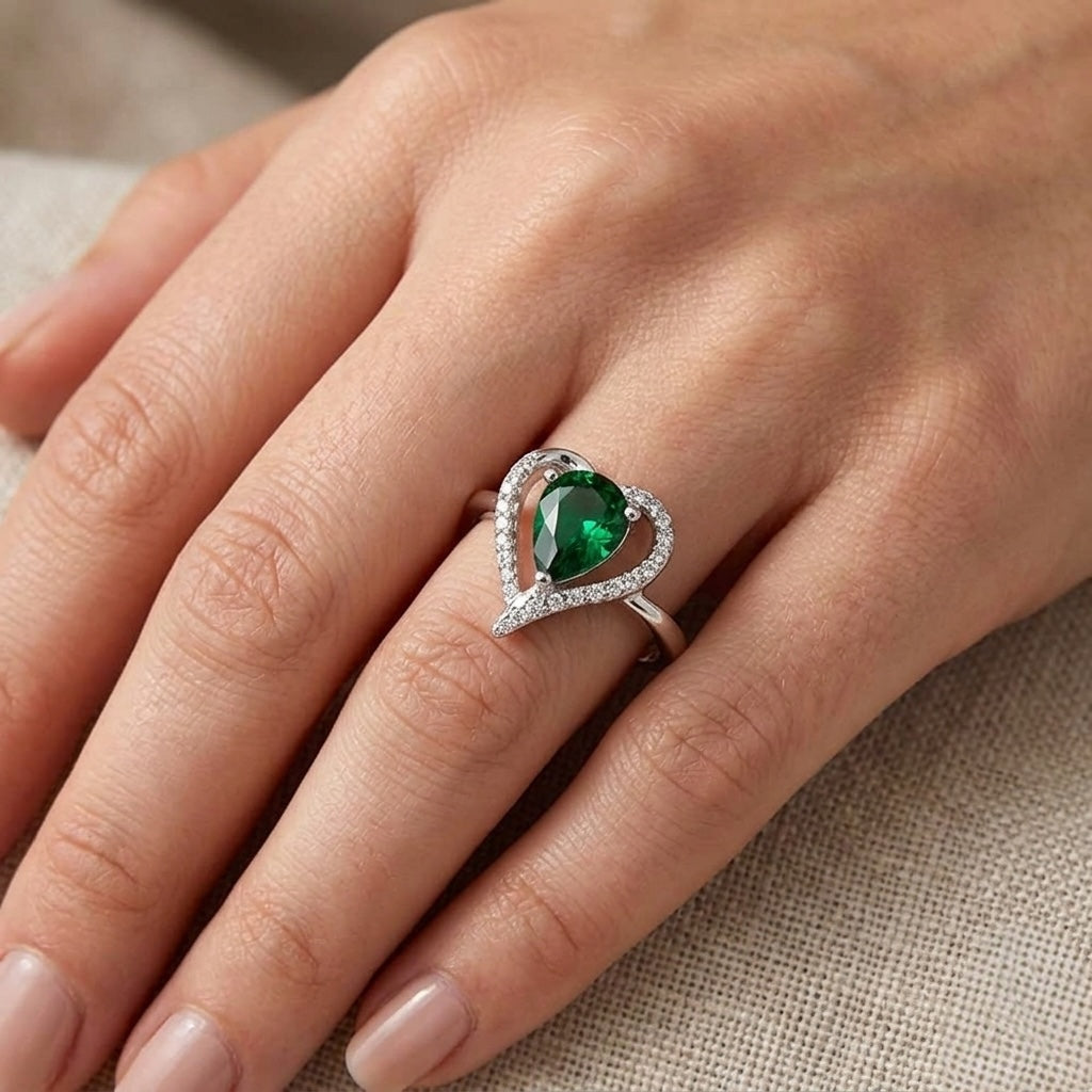 Heart-shaped emerald ring on a hand with beige fabric background