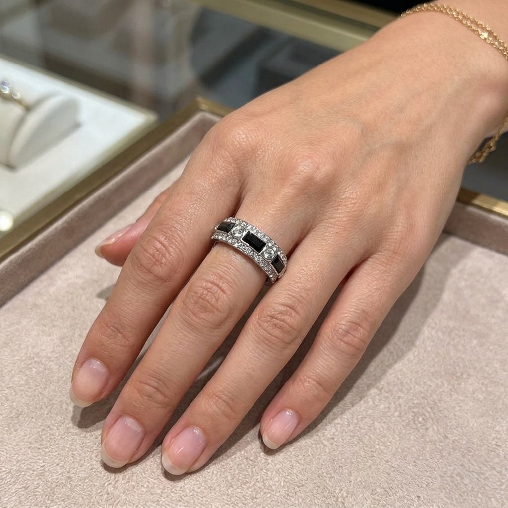 Hand wearing a silver ring with a black gemstone on a neutral background