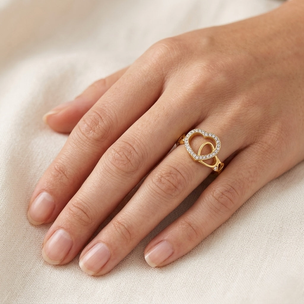 Gold ring with heart design on a hand against a beige background