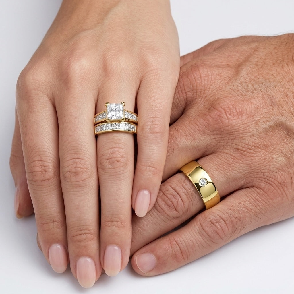 A woman's hand wearing a wedding ring set on top of a man's hand wearing a wedding band on a white background. 